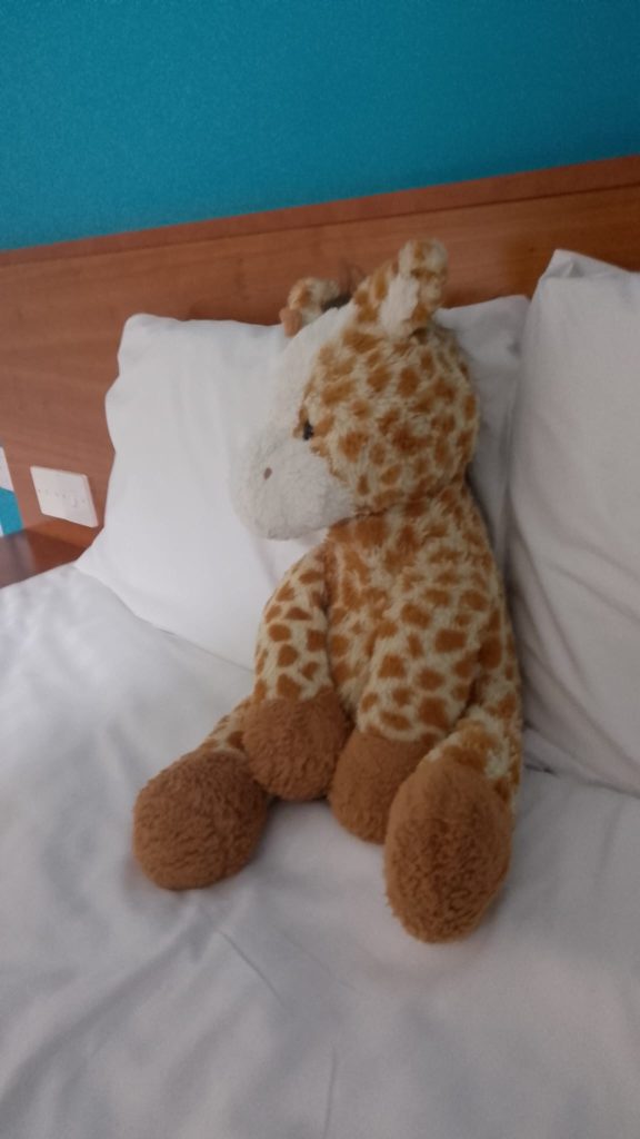An image of an adorable giraffe pluchie with a white fluffy face, a pensive expression and a combination of brutal snark and complete vulnerability.
